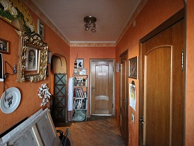 декоративная белая тарелка, фотографии в рамках под стеклом, большой цветной веер на стене коридора с коричневыми обоями трехкомнатной квартиры в жилом доме