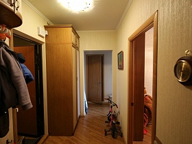 настенная вешалка, большой шкаф для одежды и детский велосипед в прихожей простой двухкомнатной квартиры