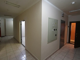 белые стены потолок, белая квадратная плитка на полу просторного холла с квартирами на этаже жилого дома