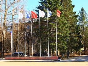 флагшток на фоне высоких зеленых елей и двухэтажного жилого дома в городке Сычево для аренды для съемок кино