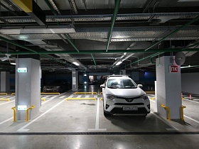 машины на размеченных местах между парковочными столбиками и желтыми ограничителями в современном интересном подземном паркинге