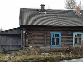 бревенчатый барачный дом с печным отоплением на несколько хозяев с голубыми наличниками на окнах во дворе за невысоким плетенным забором в Акуловке