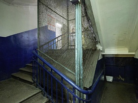 лестница с синими перилами вокруг защитной металлической сетки в коммунальном общежитии