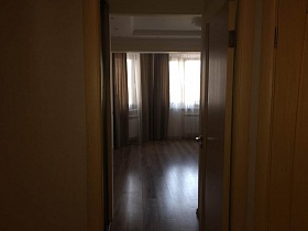 коричневая открытая дверь в просторную гостиную с коричневыми шторами на эркерных окнах семейной квартиры