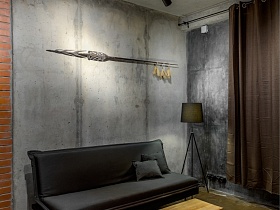журнальный стол, серый мягкий диван на ножках у бетонной стены с тремпелями на горизонтальной перекладине в студии лофт в стиле хай тек
