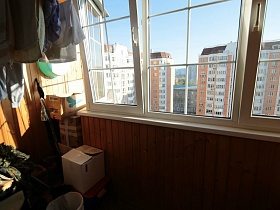 белье на веревке и многочисленные коробки на застекленном балконе трехкомнатной квартиры в многоэтажном доме