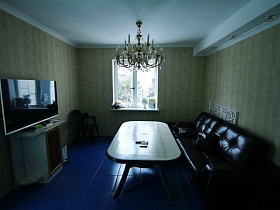 большая люстра, стилизованная под свечи на белом потолке гостиной уютного дома с яркой кухней для съемок кино