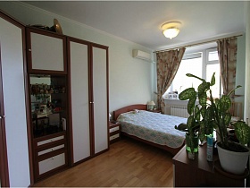комнатные цветы на комоде напротив большого углового шкафа с белыми дверцами в спальной комнате простой квартиры на Садовом