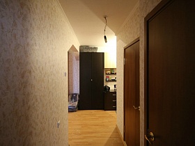 вид из коридора на коричневый шкаф для одежды, комод и навесные полочки в прихожей большой трехкомнатной квартиры в переезде