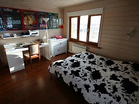 белый письменный стол и комод у стены с разноцветными плакатами в спальне деревянного современного дома