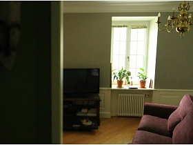 люстра, стилизованная под свечи над фиолетовым диваном в гостиной зоне стильной двухкомнатной квартире жилого дома