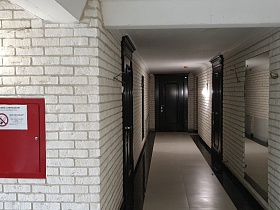 современный стильный подъезд в светло-серых тонах, с указателем на входе, прямоуголным зеркалом на кирпичных стенах и входными дверьми в квартиры жилого дома
