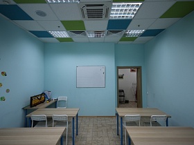 белая доска на стене, большие деревянные счеты на столе воспитателя, ряды учебных столов в просторном светлом классе детского сада