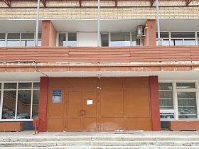 коричневая урна, бетонные цветники у входных дверей в двухэтажное здание столовой с большими окнами на фасаде и открытым длинным балконом