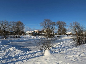 заснеженные крыши домов в деревне у пруда в зимнее время