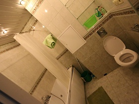 зеленое ведро и швабра, зеленый коврик у белой ванны с белой шторкой, белый санузел в ванной комнате с белой и зеленой плиткой на стенах