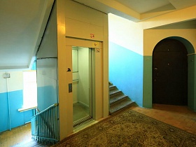 прозрачные двери лифта на лестничной клетке с голубыми панелями в жилом доме