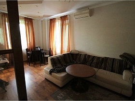 крулый журнальный столик у бежевого углового дивана с полосатыми подушками в гостиной семейной трешки сталинского двора
