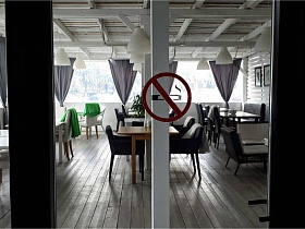 круглый красный запрещающий знак"не курить" на входных стеклянных раздвижных дверях уютного кафе с большими окнами