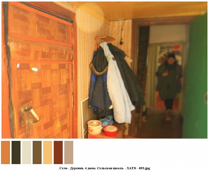 одежда на настенной вешалке, посуда на тумбочке за общитой входной дверью прихожей жилого дома в деревне