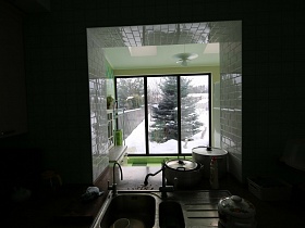 зеленая пушистая ель на участке под снегом через оконный проем яркой кухни