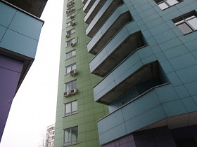 вид снизу на современные высотные дома с фиолетово-зеленым и голубым цветом стен и кондиционерами под окнами