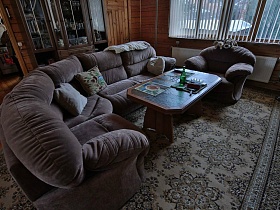 деревянный журнальный столик с салфетками у серого мягкого дивана с подушками на цветном ковре по центру гостиной современной уютной загородной дачи