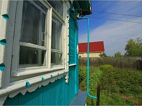 белые деревянные рамы на окнах голубой старой дачи СССР за высоким штакетным забором у поля