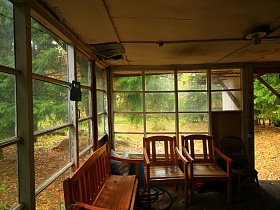 разрушенный крагис потолка застекленной веранды с выбитым окном в бедном жилом домике на участке с зелеными елями у пруда