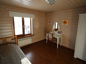 белый шкаф для одежды, белый гримерный столик с круглым зеркалом в рамке у стены с цветочными картинами в спальне просторного деревянного дома