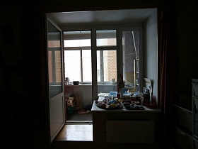многочисленные предметы, необходимые вещи на широком подоконнике окна с дверью на застекленный балкон трехкомнатной семейной квартиры