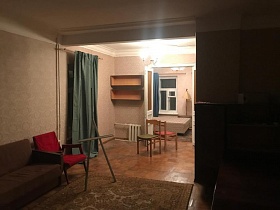 два старых деревянных стула на полу с квадратами смежной комнаты с навесными книжными полками и темной шторой на бежевой стене из открытого дверного проема гостиной квартиры на Остоженке