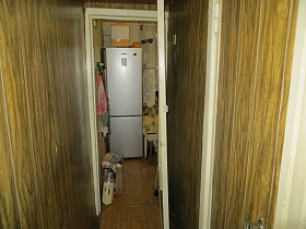 термос, набитая картонная коробка у стены с полотенцами на крючках вешалки, белый двухкамерный холодильник на кухне из открытой прихожей квартиры советской эпохи