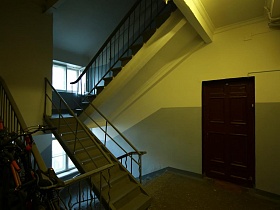 велосипеды, пристегнутые к металлическим перилам винтовой лестницы на площадке этажа отремонтированного подъезда с жилыми квартирами дома эпохи СССР