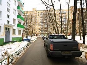 ряд машин на проезжей дороге у красивого дома с зелеными балконами