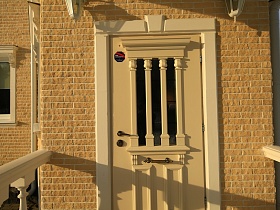 деревянная бежевая входная дверь с имитацией колон на стекле на крыльце современного загородного дома