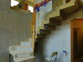 барный стул под витой бетонной лестницей с дождиком на деревянных перилах, ведущей на второй этаж просторной квартиры без ремонта для съемок кино