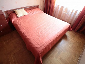большая деревянная кровать с розовым стеганным одеялом и белой подушкой в спальной комнате трешки