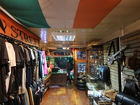 стойка с одеждой на тремпелях, шины и диски на колеса мотоцикла, гитары, сумки на деревянной стене небольшого магазина мотошмоток