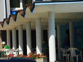 уютные столики со стульями для отдыхающих на открытой террасе с белыми круглыми колонами под волнистой крышей гостиницы "Дубна" советского времени