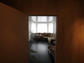 комнатный цветок, бежевое мягкое кресло и угловой диван у большого эркерного окна современной квартиры на первом этаже из открытой двери прихожей