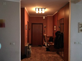 деревянный диванчик, шкаф под потолок для одежды с зеркальными дверцами, обувь на коврике у входной двери в коричневую прихожую квартиры бухгалтера