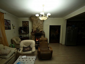 белая люстра в просторной гостиной с мягкой мебелью и камином в зонированой комнате простого семейного дома в глухом лесу