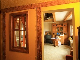 песочного цвета стены с деревянной отделкой комнаты с деревянным окном и открытым дверным проемом в гостиную