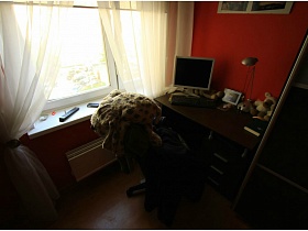 монитор компьютера, настольная лампа и фотография в рамке на столе у окна спальни с белой гардиной современной трехкомнатной квартиры