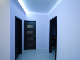 светлый коридор с черными дверьми в комнаты, натяжным потолком с подсветкой и светлым полом