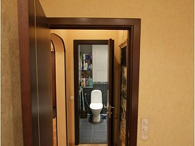 белый санузел на полу с серой квадратной плиткой ванной комнаты через открытые двери из спальной комнаты простой двухкомнатной квартиры с хорошим подъездом