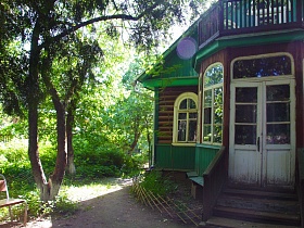 белые входные двери с потрескавшейся краской на деревянном крыльце с перилами на веранду художественной дачи-музей с зеленым участком