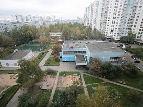 вид из окна простой семейной квартиры на детский садик с игровыми участками и зелеными  площадками среди жилого квартала
