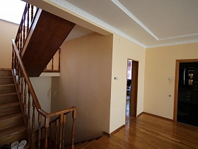 бежевые стены просторного холла и стен у деревянной лестницы с резными перилами между этажами семейной уютной дачи с видом на городские кварталы